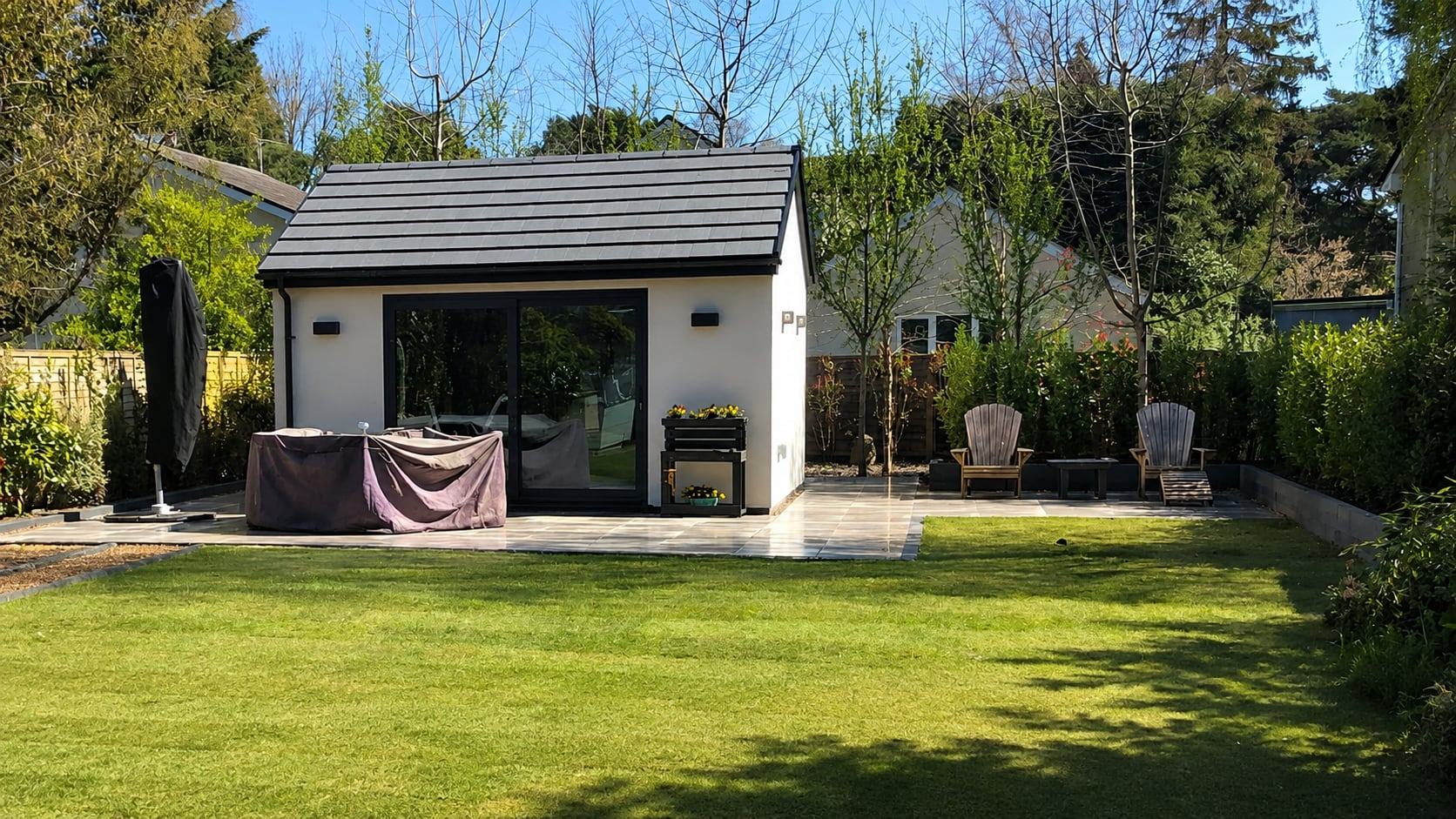 After: porcelain patio around a garden room with a new striped lawn, Dorset