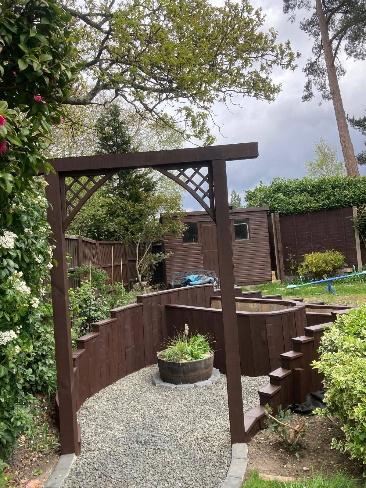 Curved raised sleeper veggie beds and amphitheatre-style seating with gravel paths and a pergola arch