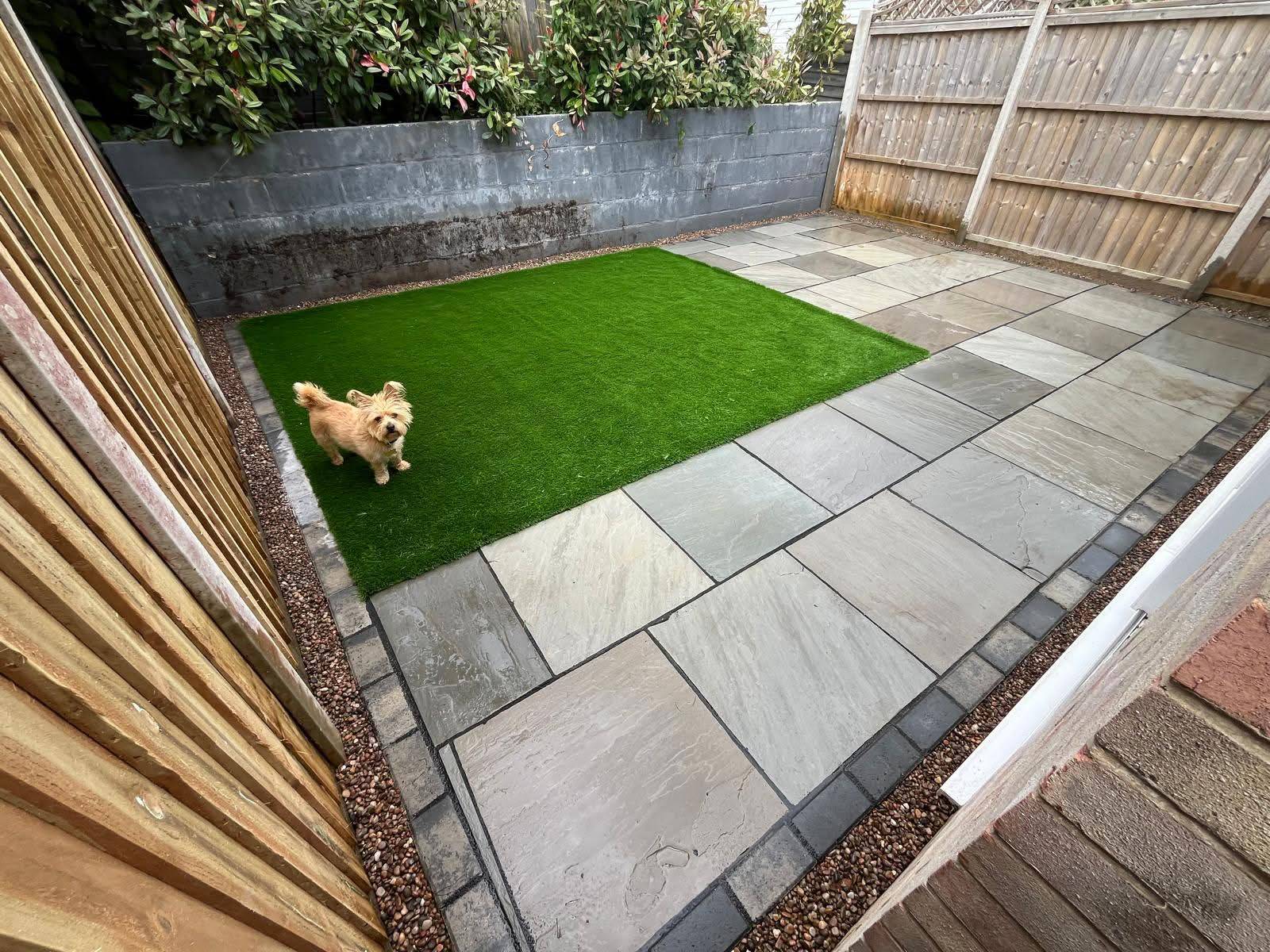 Small enclosed garden with Carbon Indian Sandstone patio, artificial grass and a new supporting wall